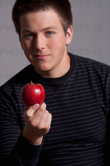 Portrait of teenage boy (16-17) with red apple, studio shot. Photo: Rob Lewine