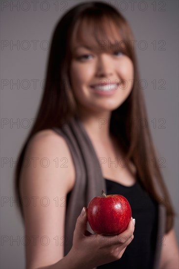 Portrait of teenage girl (16-17) with red apple, studio shot. Photo: Rob Lewine