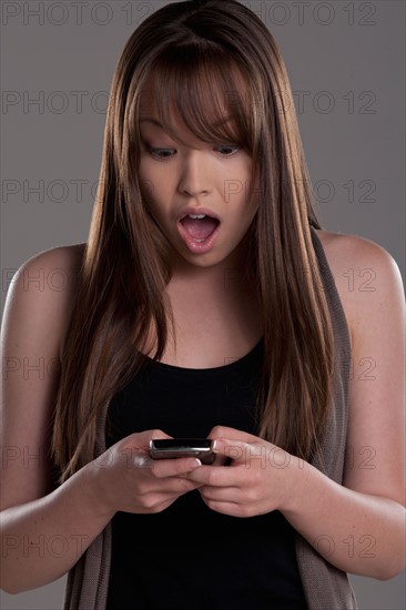 Portrait of teenage girl (16-17) with mobile phone, studio shot. Photo: Rob Lewine