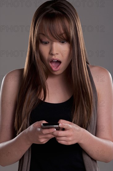 Portrait of teenage girl (16-17) with mobile phone, studio shot. Photo : Rob Lewine