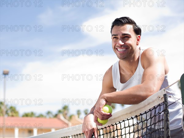 Smiling man standing near tennis net. Photo : db2stock