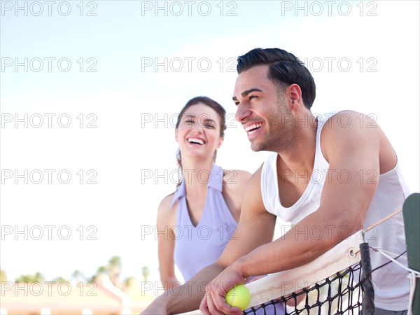 Smiling couple standing near tennis net. Photo : db2stock