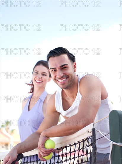 Smiling couple standing near tennis net. Photo : db2stock