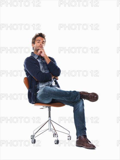 Studio shot of young pensive man sitting on chair. Photo: momentimages