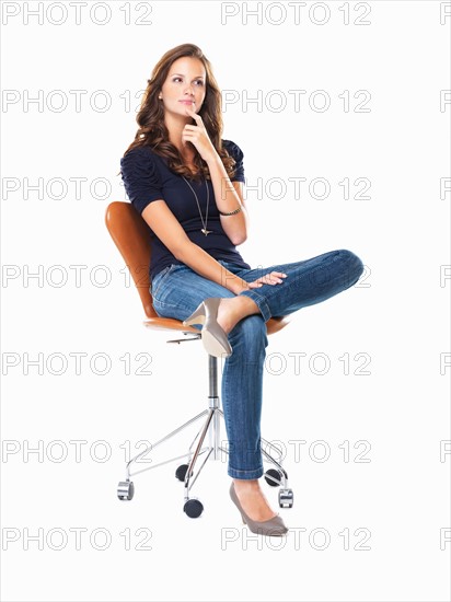 Studio shot of young woman sitting on chair and thinking. Photo: momentimages