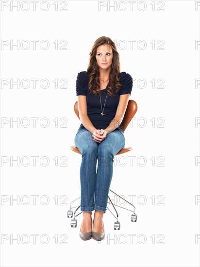 Studio shot of young woman sitting on chair with hands clasped. Photo : momentimages