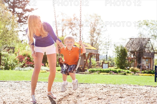 USA, Washington State, Seattle, Mother and son (2-3) swinging on swing in park. Photo: Take A Pix Media