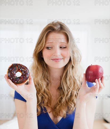 Young woman choosing between donut and apple. Photo : Jamie Grill