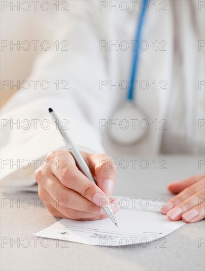 Close up of female doctor's hands writing prescription. Photo : Jamie Grill