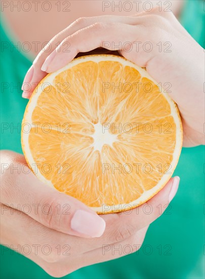 Close up of woman's hands holding half of orange. Photo : Jamie Grill