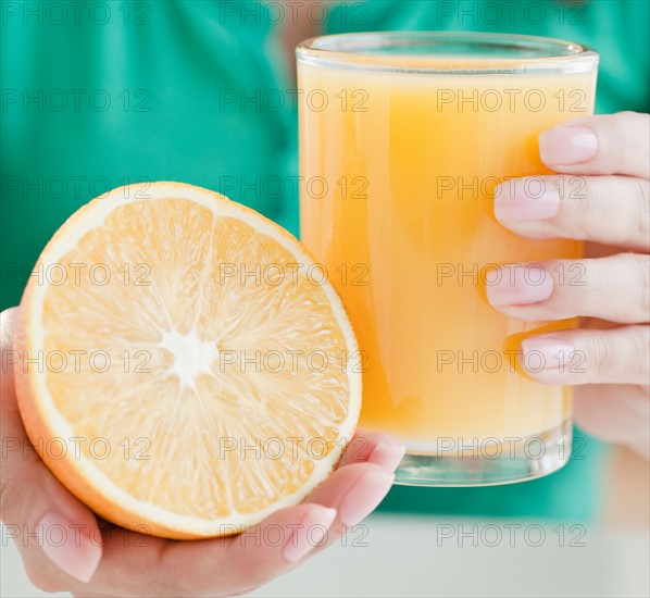 Close up of woman's hands holding half of orange and glass of juice. Photo : Jamie Grill