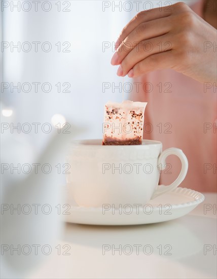 Close up of woman's hand putting teabag into tea cup. Photo: Jamie Grill