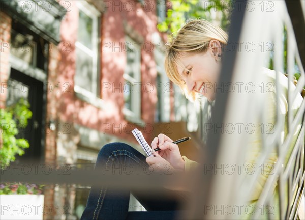 USA, New York, Williamsburg, Brooklyn, Smiling woman writing diary. Photo: Jamie Grill