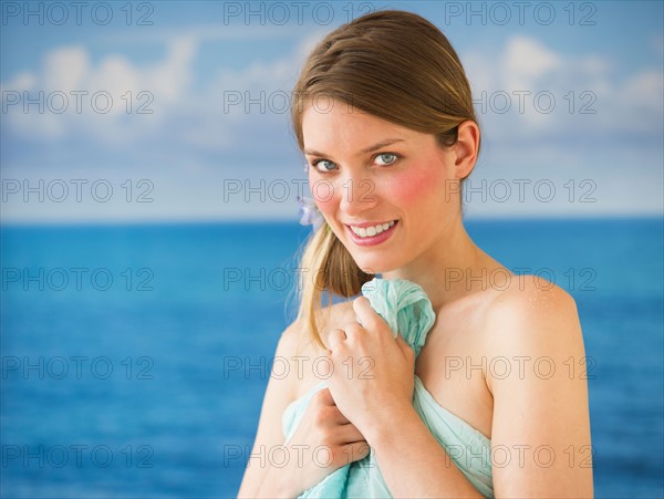 Portrait of young woman holding towel by sea.