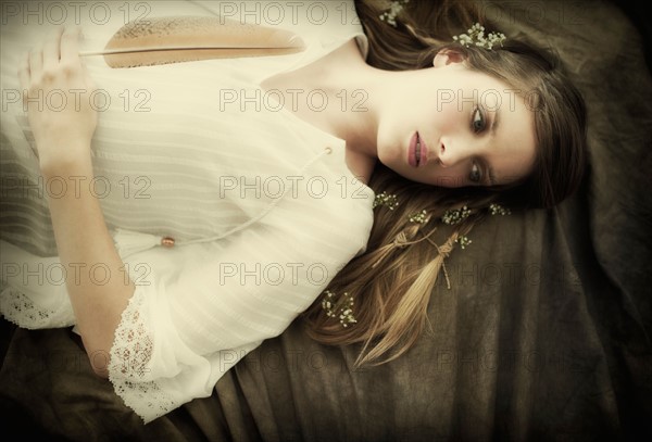 Young woman holding feather lying on back.