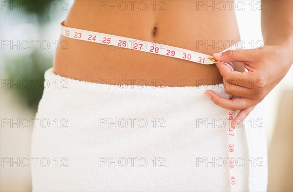 Midsection of woman measuring waist.