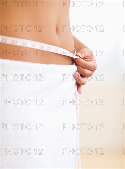 Midsection of woman measuring waist.