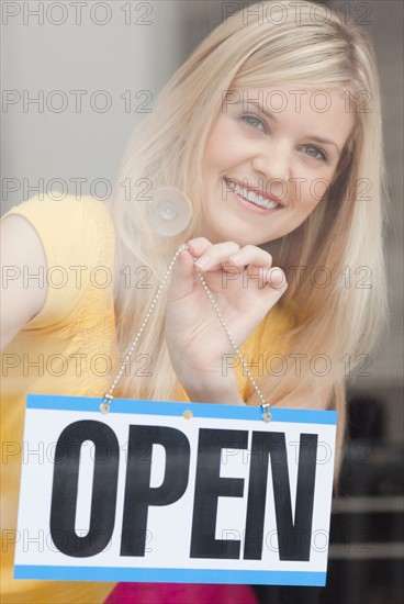 Portrait of young woman hanging sign in window. Photo : Jamie Grill