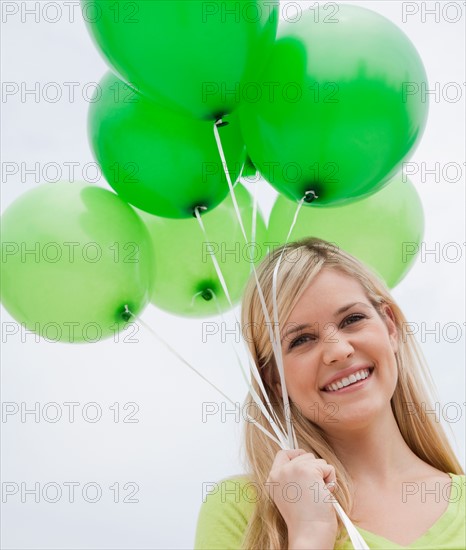 Portrait of young woman holding green balloons. Photo: Jamie Grill