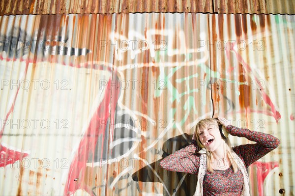 USA, Brooklyn, Williamsburg, Portrait of woman with headphones against graffiti wall. Photo : Jamie Grill