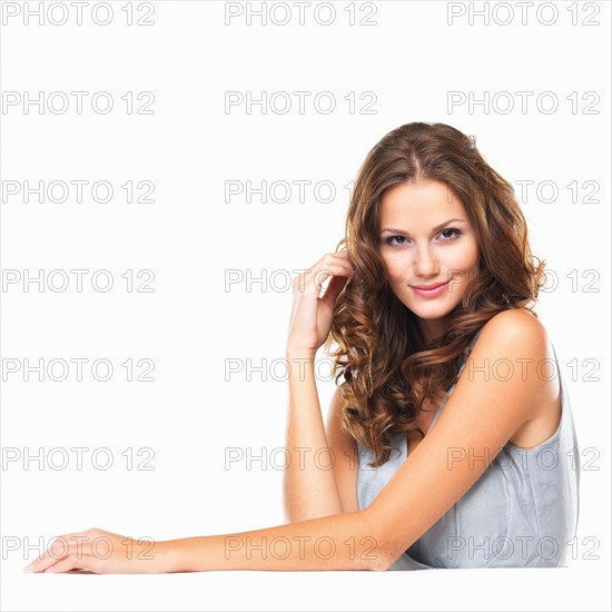 Studio portrait of young woman sitting at table and smiling. Photo : momentimages