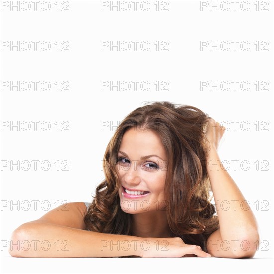 Studio portrait of young woman sitting at table and smiling. Photo : momentimages