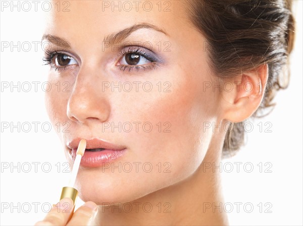 Studio portrait of beautiful woman applying lip gloss. Photo : momentimages