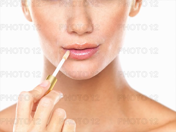 Studio portrait of beautiful woman applying lip gloss. Photo : momentimages