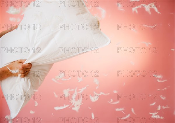 Close up of hands holding pillow with feathers flying around. Photo : Jamie Grill