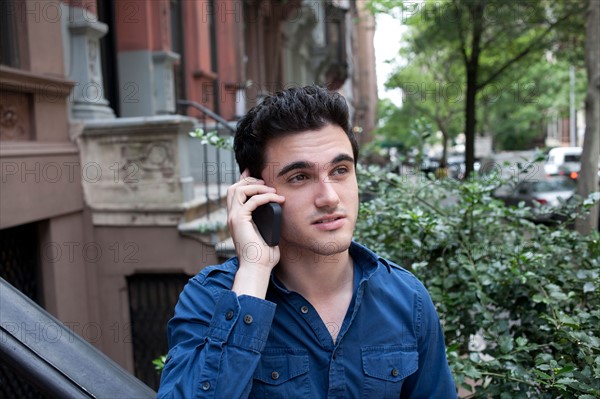 USA, New York, New York City, Young man talking on mobile phone on street. Photo : Winslow Productions