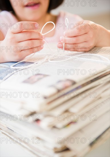 Girl's (8-9) hands tying pile of newspapers with string. Photo: Jamie Grill