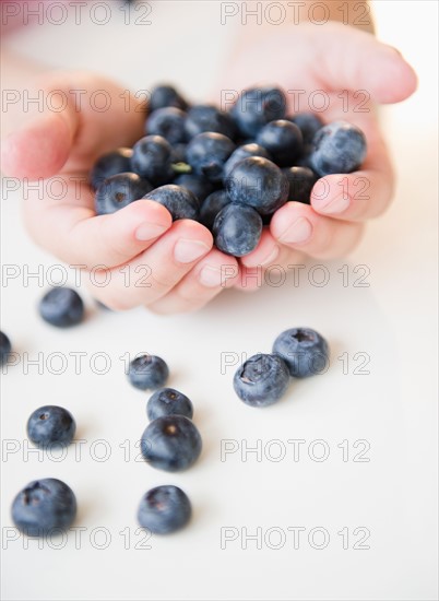 Close up of girl's (8-9) hands holding blueberries. Photo : Jamie Grill