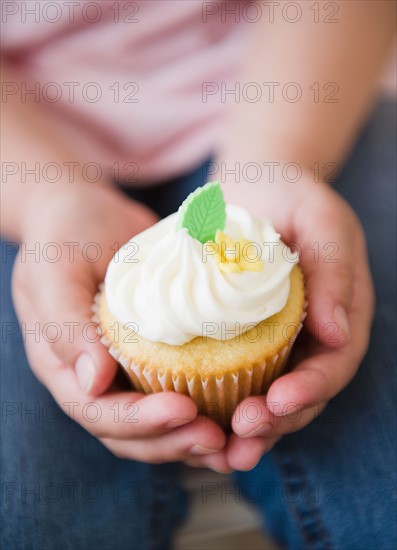 Close up of girl's (8-9) hands holding cupcake. Photo : Jamie Grill