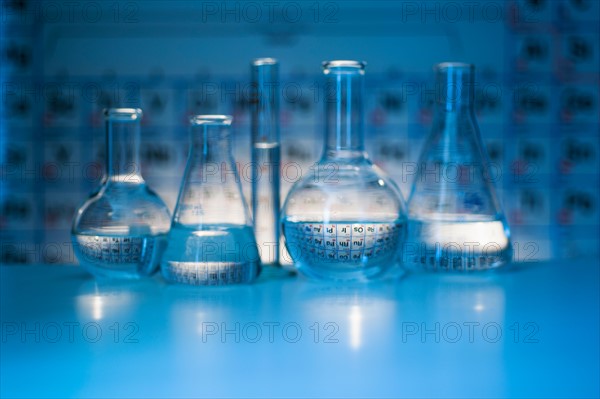 Beakers and flasks with periodic tables in laboratory.