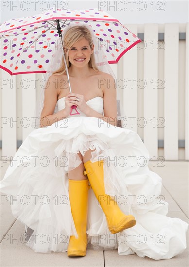 Bride sitting in yellow rubber boots with umbrella. Photo : Jamie Grill