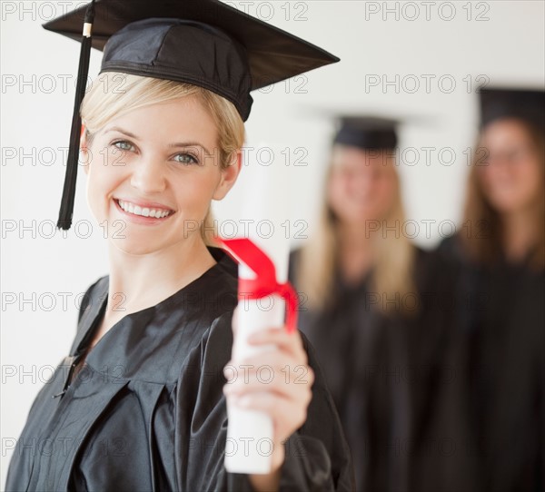 University student wearing graduation gown holding diploma. Photo : Jamie Grill