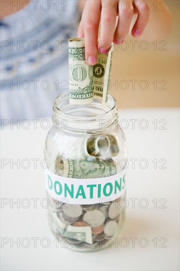 Close up of girl's (10-11) hand putting dollar bill into jar. Photo : Jamie Grill