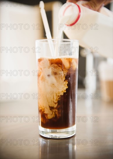 Close up of hand pouring milk into iced coffee. Photo : Jamie Grill