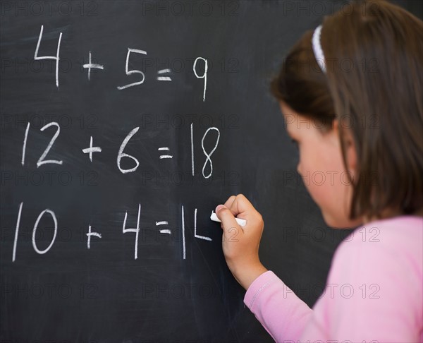 Close up of girl (6-7) writing on blackboard. Photo : Daniel Grill