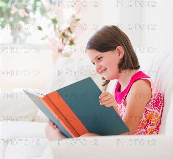 Close up of girl (6-7) reading book on sofa. Photo: Daniel Grill