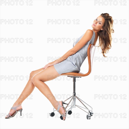 Studio shot of young woman relaxing on chair and smiling. Photo : momentimages