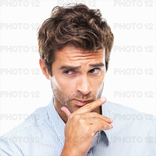 Close-up portrait of confused business man with had on chin against white background. Photo: momentimages