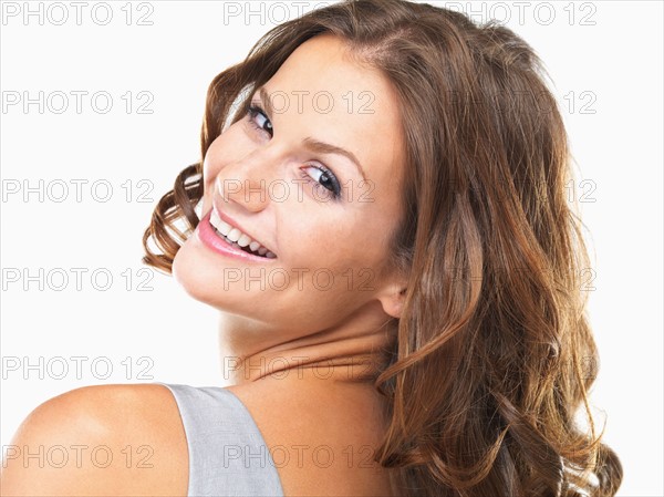 Studio portrait of young woman smiling and looking over shoulder. Photo : momentimages