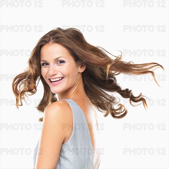 Studio portrait of young woman smiling and looking over shoulder. Photo: momentimages