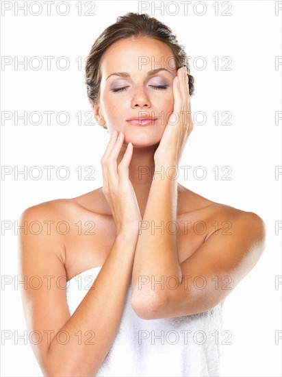 Studio portrait of beautiful woman wrapped in towel touching face. Photo : momentimages