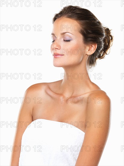 Studio portrait of beautiful woman wrapped in towel with eyes closed. Photo: momentimages
