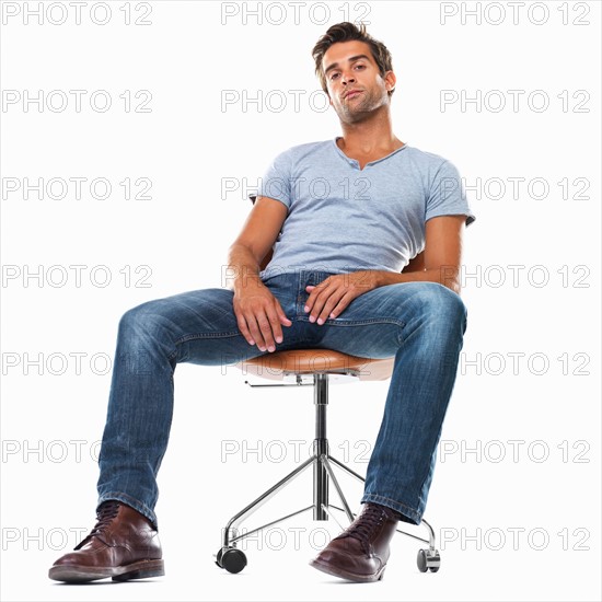 Portrait of smart young man sitting comfortably on chair against white background. Photo: momentimages