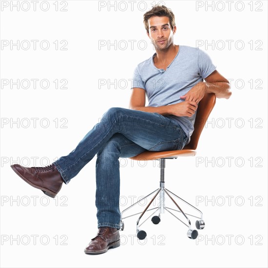 Portrait of young man sitting on chair with legs crossed against white background. Photo: momentimages