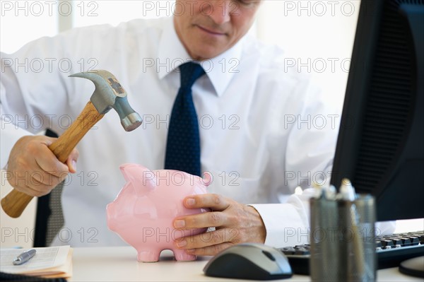 Businessman hammering piggy bank.