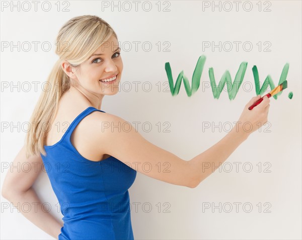 Blonde young woman writing web address on wall. Photo : Jamie Grill